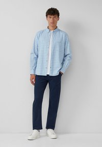 Lichtblauw geruit overhemd met knopen, een witte T-shirt met ronde hals eronder, gecombineerd met marineblauwe chinos en witte sneakers.