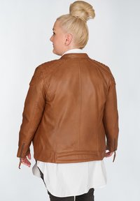Braune Lederjacke mit gesteppten Schultern, taillierten Design, Reißverschlüssen an den Ärmelbündchen und einer glatten Textur, getragen über einem weißen Hemd.