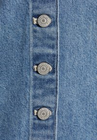 Gros plan sur un tissu denim bleu avec trois boutons métalliques Levi Strauss disposés verticalement sur une couture cousue.