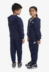 Ensemble de sweat-shirt et pantalon bleu marine, en coton, doté d'une fermeture éclair, de poches et d'accents du logo Nike sur la poitrine et la cuisse.