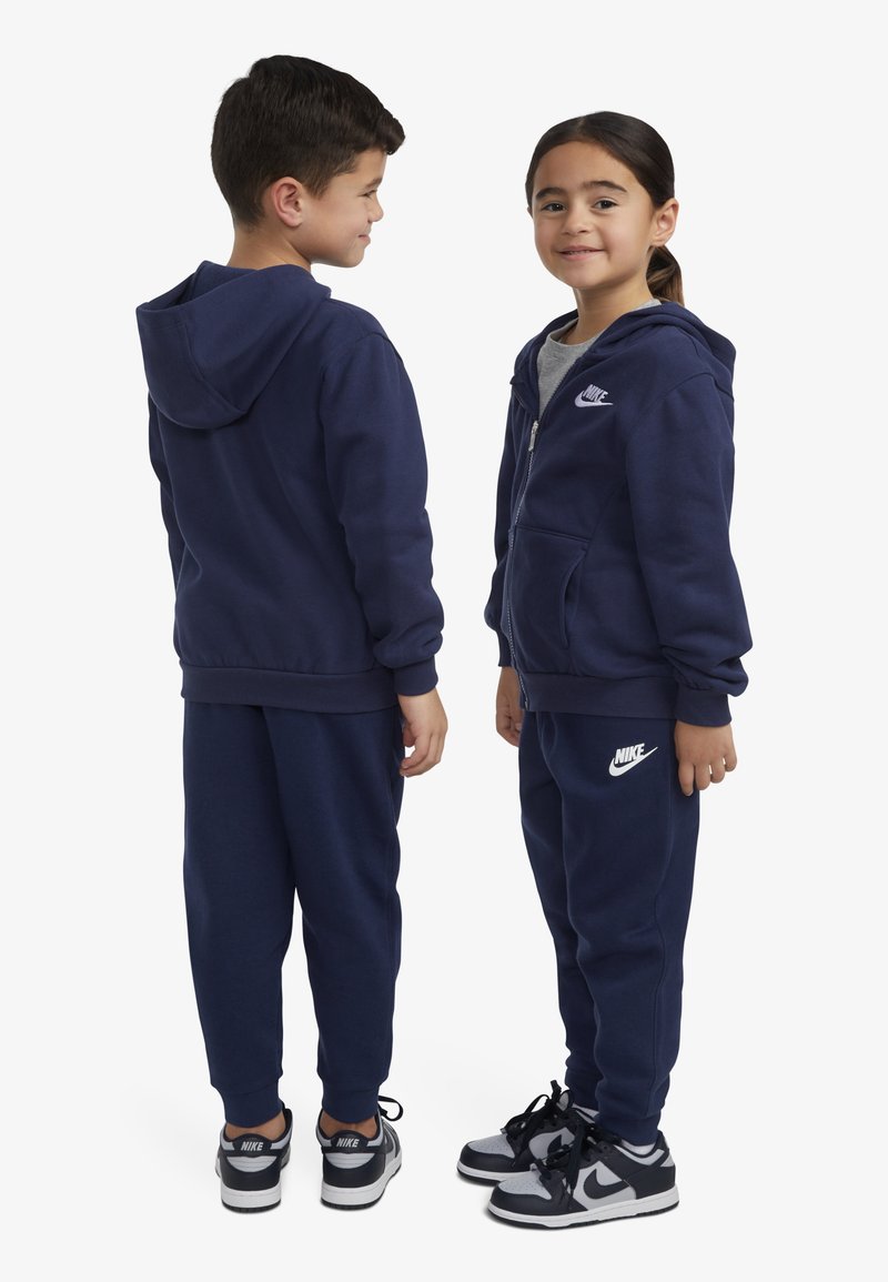 Ensemble de sweat-shirt et pantalon bleu marine, en coton, doté d'une fermeture éclair, de poches et d'accents du logo Nike sur la poitrine et la cuisse.