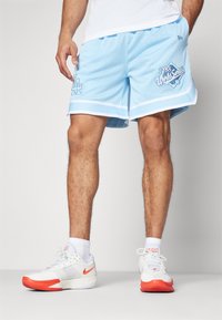 Light blue mesh basketball shorts with white trim, featuring "1988 World Series" and logo graphics on the left leg. Worn with white and red sneakers.