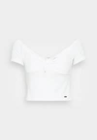 Camiseta blanca corta hecha de tela acanalada, con mangas cortas y un detalle de nudo en el frente. Diseño sencillo con una pequeña etiqueta negra en el dobladillo.