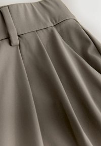 Harmaa laskostettu hame, jossa on sileä, pehmeä koostumus ja leveä vyötärönauha, jossa on solkiosio. Kangas laskeutuu pehmeästi luoden tyylikkäitä laskoksia.