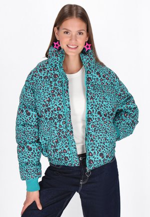 Turquoise puffer jacket with black and pink leopard print, high collar, zip closure, and contrasting cuffs. Model wears a white top and denim.