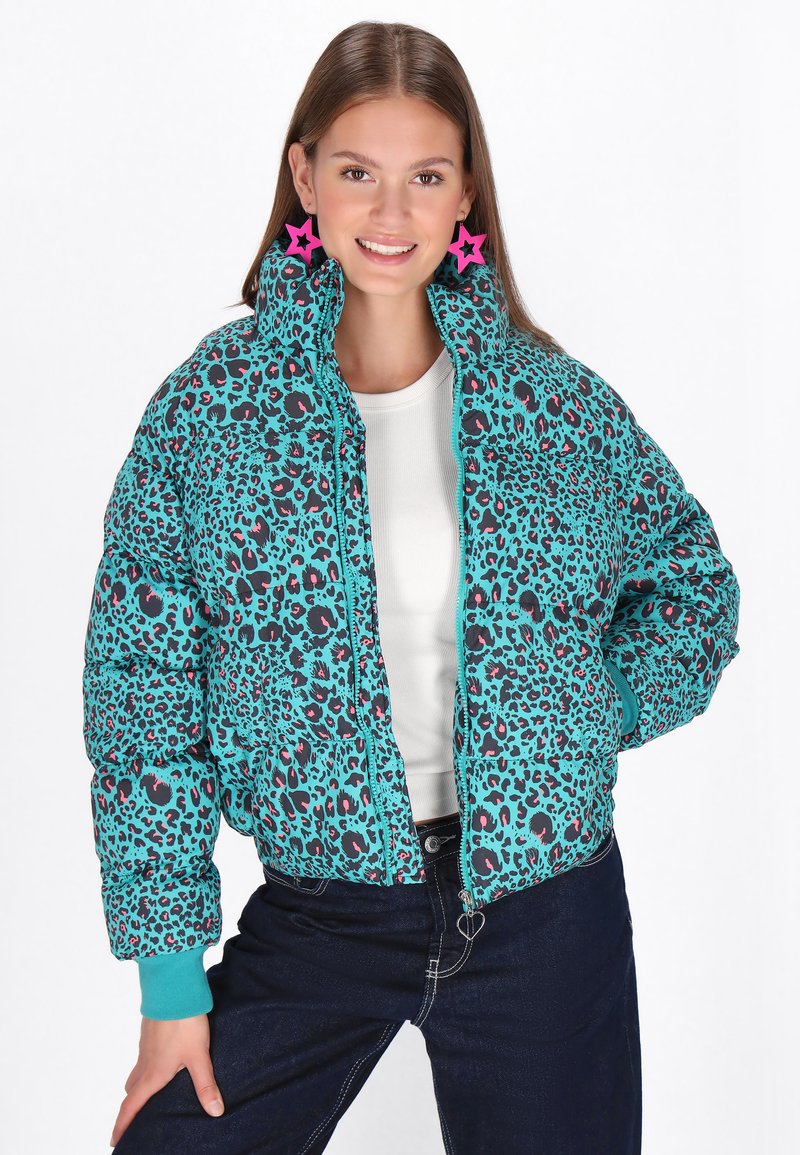 Jachetă puf turquoise cu imprimeu leopard negru și roz, guler înalt, închidere cu fermoar și mansete contrastante. Modelul poartă un top alb și blugi.