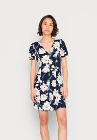 Vestido floral com fundo azul- Escuro, grandes flores brancas e folhas verdes, decote em V e mangas curtas bufantes.