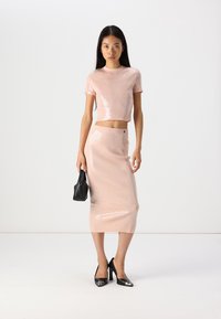 Dvoukníkový outfit v jemné růžové, skládající se z krátkého topu a midi sukně. Vyrobený z žebrovaného materiálu s lesklou texturou a diskrétním logem.