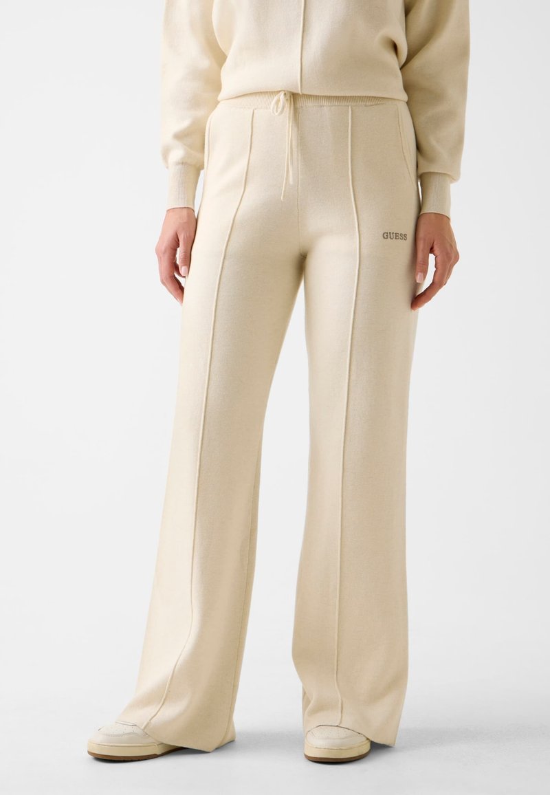 Cream-colored wide-leg sweatpants with a soft texture, featuring tonal stitching and a small "GUESS" logo on the left hip.