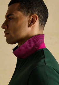 Roheline särk kõrge kraega, millel on roosa ja lilla horisontaalsed triibud. Kangas näeb välja sile ja struktureeritud disainiga.