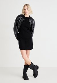 Black leather bomber jacket over a fitted black dress. Knee-high black boots with a chunky sole. Simple, sleek lines and minimal detailing.