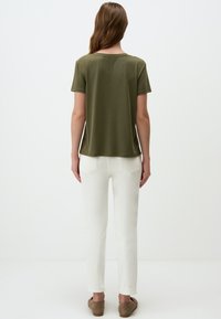 Top corto a maniche corte verde oliva con scollatura rotonda, vestibilità comoda e dettagli discreti sull'orlo, abbinato a jeans bianchi aderenti e scarpe beige.