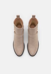 Beige suede ankle boots with a smooth texture, rounded toe, and a side buckle detail. Low black rubber heel and pull tab at the back.