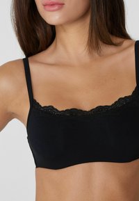 Černý bralet s nastavitelnými ramínky, zdobený skalní krajkovou lemovkou kolem výstřihu a jemnou, hladkou texturou látky.