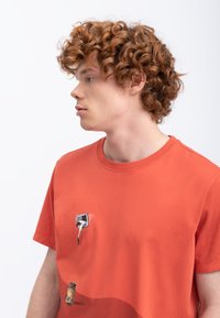 Oranje katoenen t-shirt met een afbeelding van een kraan en een vat, met een ronde halslijn en korte mouwen. Textuurontwerp voegt detail toe.