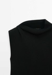 Haut noir sans manches en maille avec un col roulé large et doux, présenté à plat sur un fond blanc.