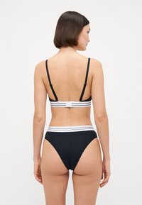 Svart bikini topp med tynne stropper og lukking bak, kombinert med høy-midje truser med en hvit stripet midjebånd.