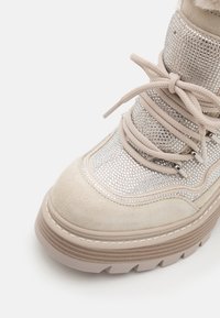 Beige ruskinds ankelstøvle med en skinnende, sølv rhinestone-overdel, tyk gummisål og snørebånd. Har teksturerede detaljer og polstret krave.