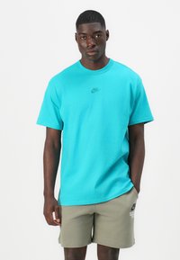 Turkis kortermet t-skjorte med Nike-logo på brystet, kombinert med khakifargede shorts. T-skjorten har en avslappet passform og myk tekstur.