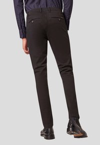 Zwarte broek met een slim fit, met achterzakken en een gladde textuur. Gecombineerd met glanzende zwarte schoenen. Eenvoudig en modern ontwerp.