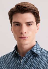 Camicia in tessuto blu scuro con un motivo di piccoli cerchi azzurri. Ha un colletto a punta e una patta con bottoni.