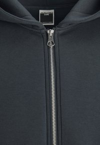 Sweat à capuche noir zippé avec fermeture éclair en métal argenté et étiquette "Jack & Jones Core" à l'intérieur du col, présenté en gros plan.