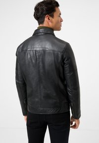 Schwarze Lederjacke mit strukturiertem Kragen und Reißverschluss-Ärmeln. Glatte Textur und taillierte Passform, kombiniert mit schwarzen Jeans.