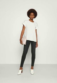 Top branco de mangas curtas com costura lateral, combinado com jeans skinnies pretos e mules brancos de salto. Segura uma clutch rosa claro.