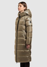 Lange olijfgroene gewatteerde jas met een glanzende afwerking, horizontale stiksels, ritssluiting, grote capuchon en zijzakken.