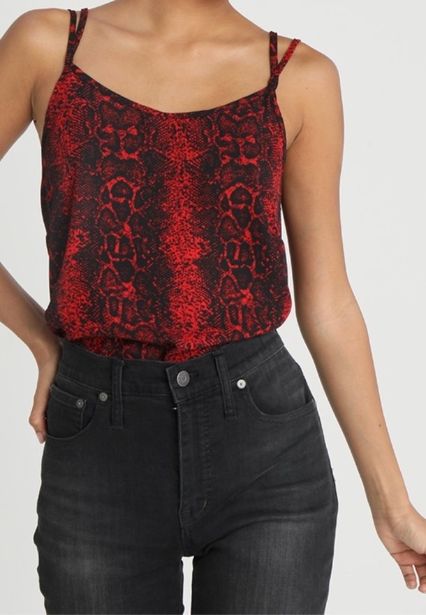 Camisole imprimé serpentin rouge et noir avec fines bretelles, associée à un jean en denim noir taille haute avec poches avant et boutons.