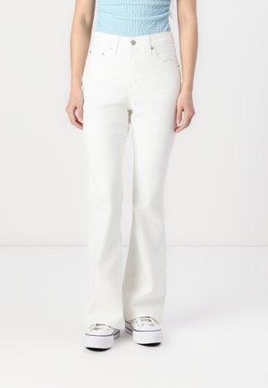 Personne portant un jean blanc flare taille haute, un top sans manches bleu clair texturé et des baskets blanches à plateforme sur fond blanc uni.