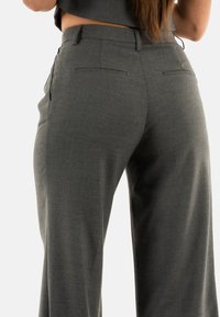 Pantaloni grigi su misura con una texture liscia, design a gamba dritta e tasche posteriori, posizionati su uno sfondo bianco.