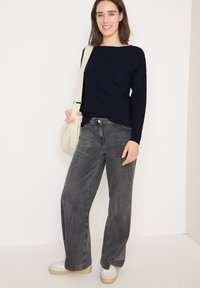 Granatowy prążkowany top z długim rękawem, szare jeansy typu wide-leg z kieszeniami i jasne sneakersy. Modelka trzyma kremową torbę na ramię.