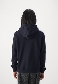 Sweat-shirt à capuche bleu marine à manches longues, en mélange de coton, avec une poche kangourou et des bandes latérales blanches contrastantes.