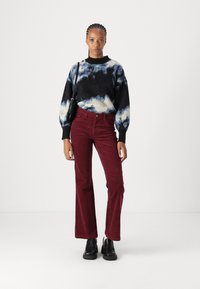 Gebreide trui met zwart, blauw en crèmekleurig golvend patroon, gecombineerd met crimsontikket flared broek. Zwarte enkellaarzen en een kleine zwarte tas.