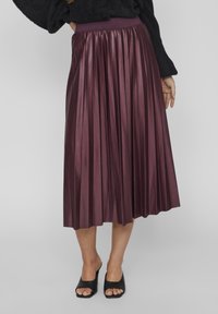 Szilva színű, plisszírozott midi szoknya, puha textúrával, széles derékrészen. Nyitott orrú fekete mules cipővel viselve, amely letisztult, elegáns dizájnt mutat.