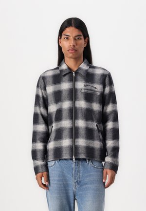 Black and white plaid jacket in a zip-up design. Made of thick fabric with a collar, side pockets, and slight texture.