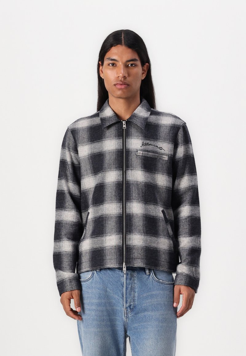 Black and white plaid jacket in a zip-up design. Made of thick fabric with a collar, side pockets, and slight texture.