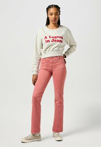 Felpa grigia chiara con testo rosso "Una leggenda nei jeans"; abbinata a jeans di denim rosa con tasche frontali e design a gamba dritta.