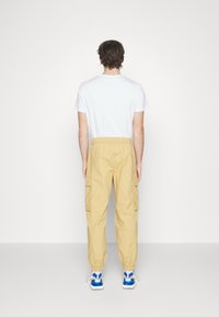 Beiga cargobyxor med sidofickor och elastiska mudd, i kombination med en vit T-shirt och flerfärgade sneakers.