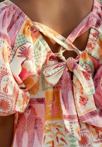 Multikleurige, lichte blouse met bloemen- en geometrische patronen, met pofmouwen en een gestrikt detail aan de achterkant.