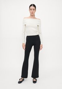 Off-shoulder witte blouse met lange mouwen in combinatie met high-waisted zwarte flared pants en zwarte ballerina's met strikaccenten.