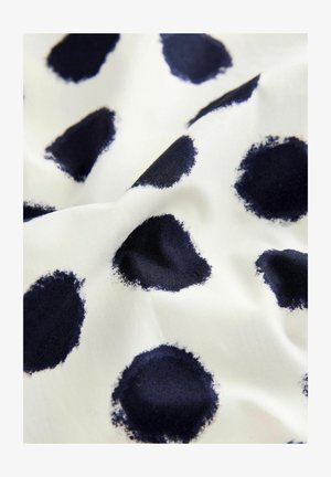 Vit tyg med stora marinblåa prickar i ett ojämnt penseldragmönster, vilket skapar en texturerad visuell effekt. Mjuk och slät textur.