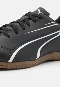 Černá sportovní obuv s bílými detaily, vyrobená ze syntetického materiálu. Obsahuje texturovanou gumovou podrážku, design na šněrování a zpevněnou špičku.