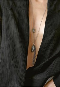 Silver necklace featuring two stones, one oval and one elongated, with a chain tassel. Worn over a textured black fabric.