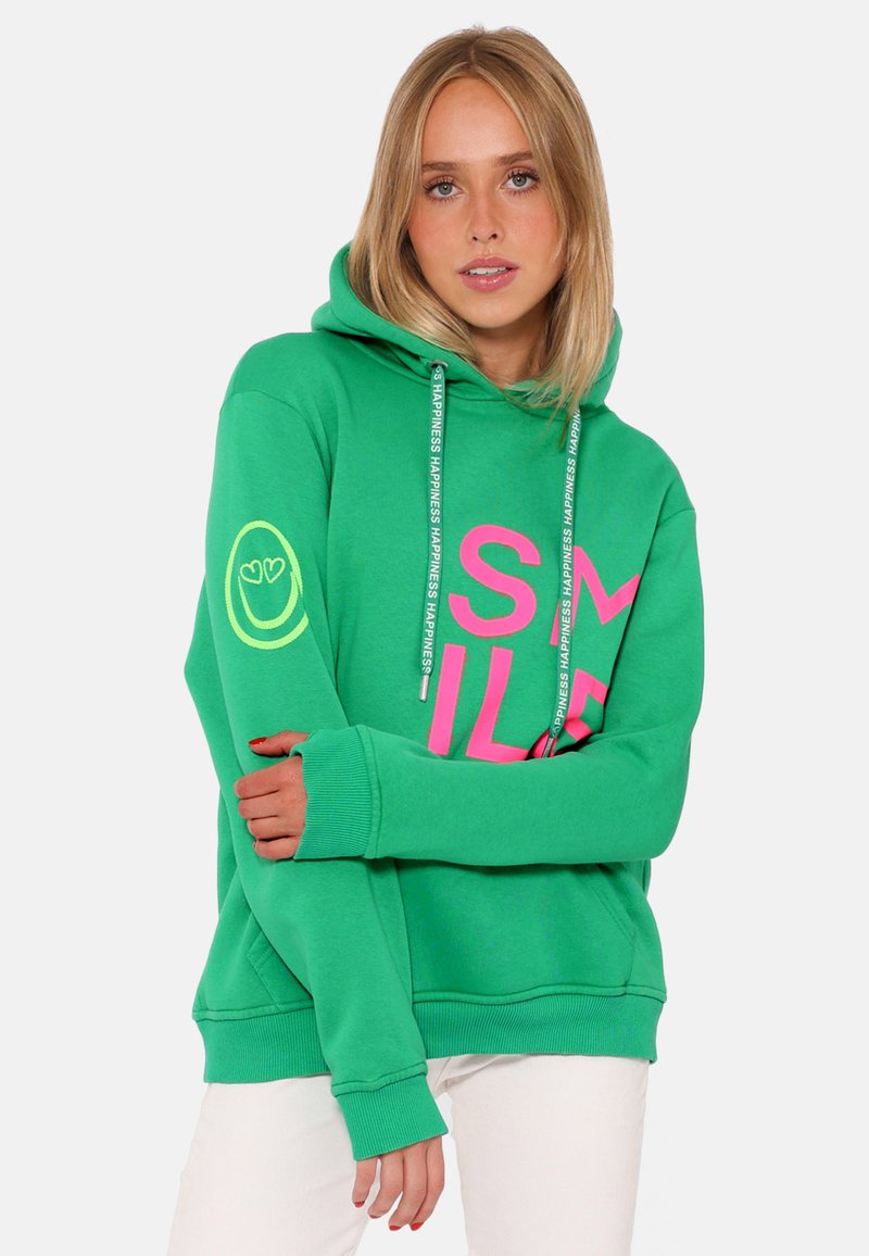Felpa verde con una grande grafica rosa "SMILE", lacci etichettati "HAPPINESS" e un faccino giallo sulla manica sinistra.