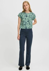 Green floral blouse with rolled sleeves paired with navy fitted trousers. The outfit features a simple design and a smooth texture.