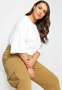 Vit oversized t-shirt med vida ärmar, tillsammans med khaki cargo-byxor med sidofickor. Mjukt tyg med avslappnad passform.