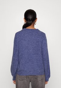 Blå stickad tröja med långa ärmar, rund halsringning och en texturerad yta. Bärs tillsammans med grå högmidjade jeans.