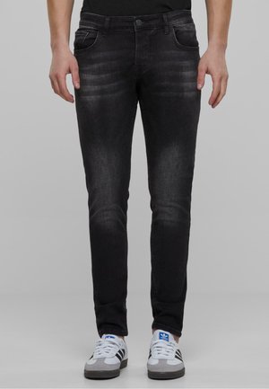 Jeans de mezclilla negra con un ajuste slim, que cuentan con un ligero desvanecimiento, cinco bolsillos y un cierre de botón. Se llevan con zapatillas gris y blancas.